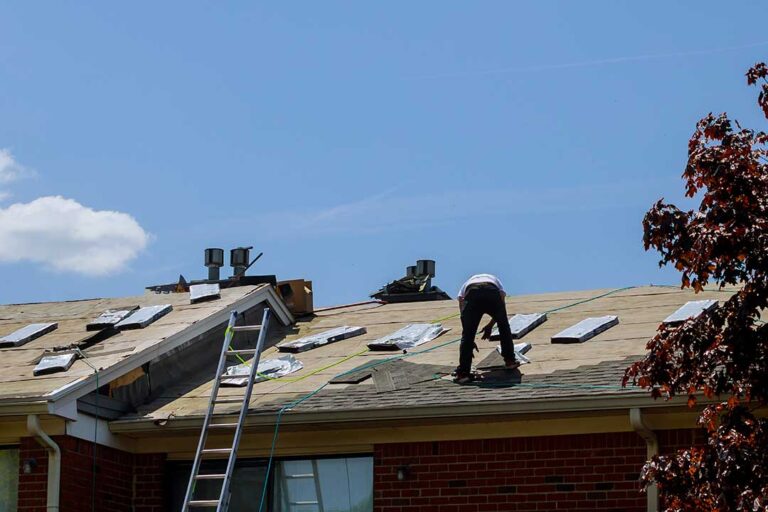 A homeowner uses a long-handled roof rake to remove snow from shingles after a winter storm.