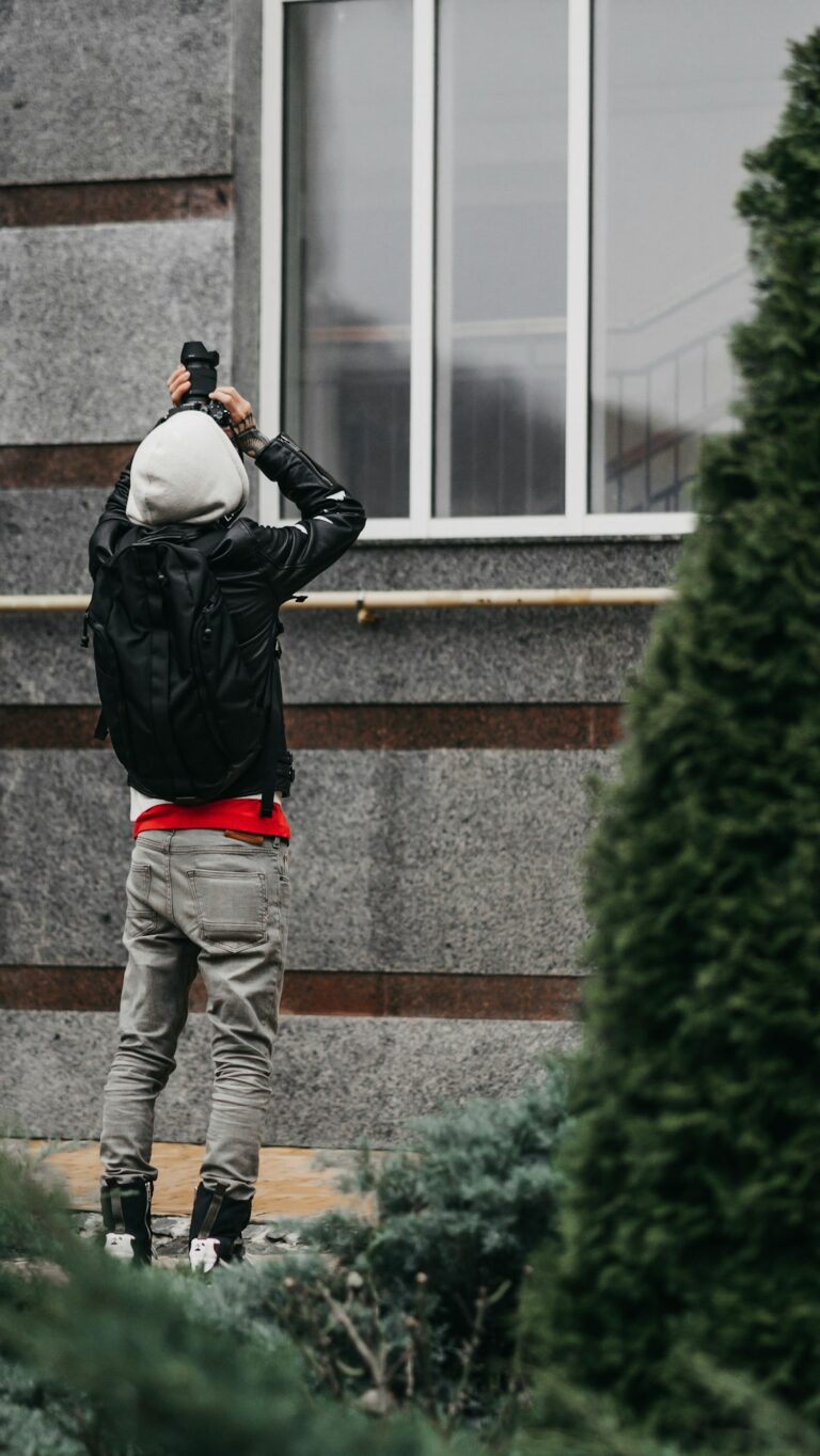 Homeowner examines a roof from the ground with binoculars after a storm while debris rests near the house.